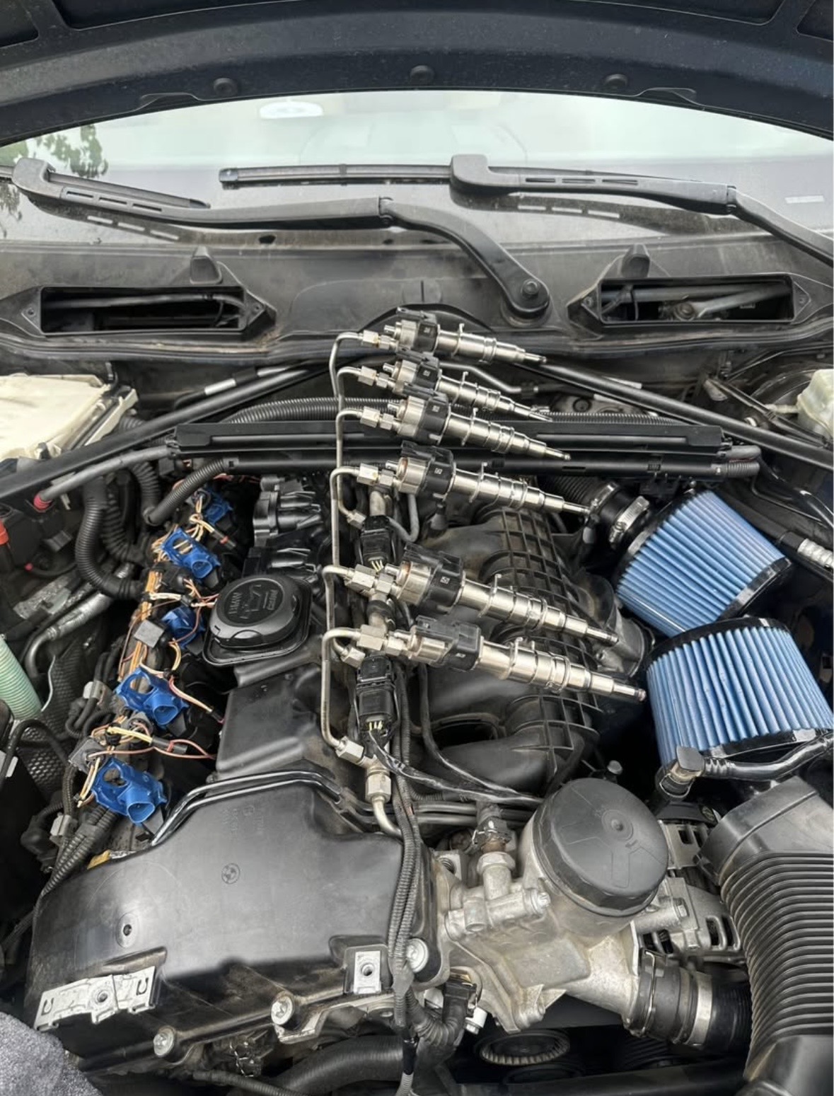 Engine bay with fuel injectors pulled and lined up on the rail, two blue cone air filters behind