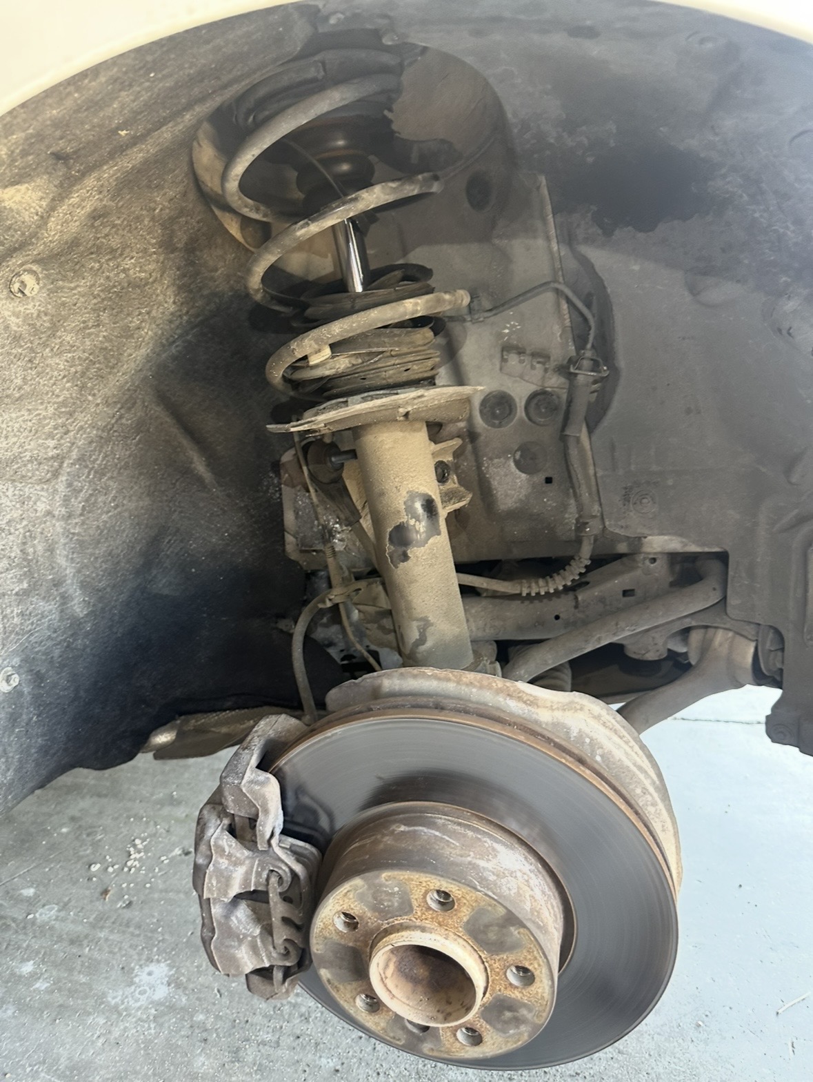 Front strut, coil spring and brake rotor exposed inside a wheel arch, wheel off