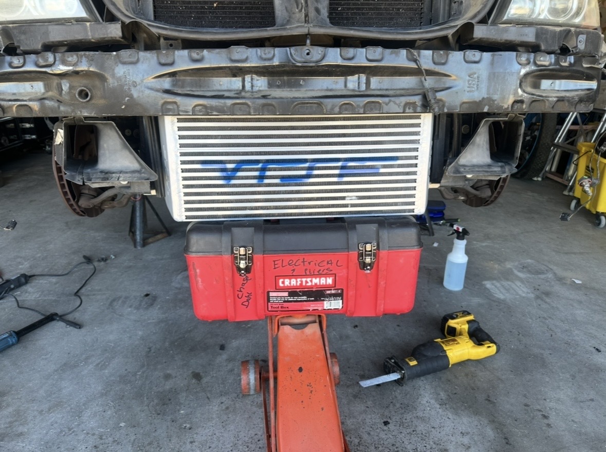 Front end of a car apart with the intercooler exposed, a red toolbox marked electrical and a floor jack in front